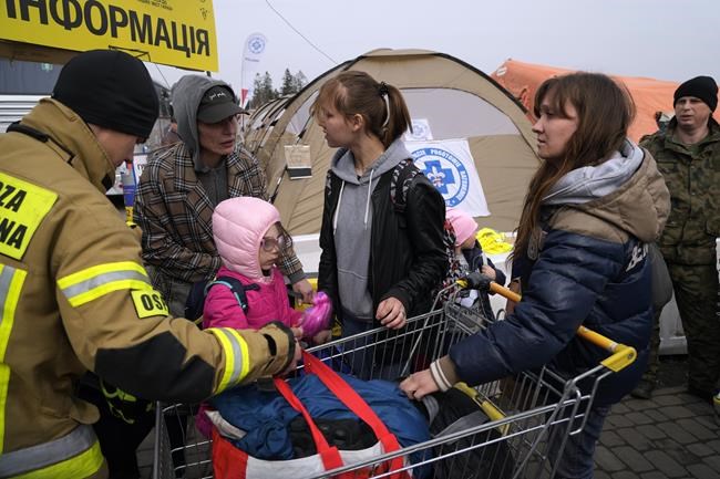 A Polish firefighter helping Ukrainian refugees, carries their belongings at border crossing in Medyka, southeastern Poland, on Wednesday, March 30, 2022. The U.N. refugee agency says more than 4 million people have now fled Ukraine following Russia's invasion, a new milestone in the largest refugee crisis in Europe since World War II. (AP Photo/Sergei Grits)