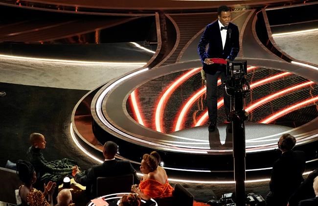 FILE - Presenter Chris Rock, right, speaks onstage as Jada Pinkett Smith and Will Smith, bottom left, look on after Smith went onstage and slapped Rock at the Oscars, March 27, 2022, at the Dolby Theatre in Los Angeles. The incident on Sunday has sparked debate about the appropriate ways for Black men to publicly defend Black women against humiliation and abuse. (AP Photo/Chris Pizzello, File)