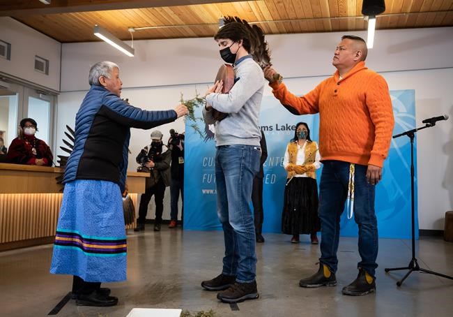 Prime Minister Justin Trudeau is touched with cedar by Charlene Belleau, left, and eagle feathers by David Archie as they perform a brushing ceremony on him during a welcoming ceremony at the Williams Lake First Nation, in Williams Lake, B.C., on Wednesday, March 30, 2022. THE CANADIAN PRESS/Darryl Dyck