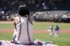 A woman sits in the outfield before a spring training baseball game between the Texas Rangers and the Los Angeles DodgersThursday, March 31, 2022, in Surprise, Ariz. (AP Photo/Charlie Riedel)