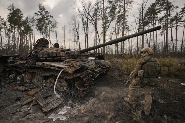 A Ukrainian serviceman stands next to a destroyed Russian tank after Ukrainian forces overran a Russian position outside Kyiv, Ukraine, Thursday, March 31, 2022. Heavy fighting raged on the outskirts of Kyiv and other zones Thursday amid indications the Kremlin is using talk of de-escalation as cover while regrouping and resupplying its forces and redeploying them for a stepped-up offensive in eastern Ukraine.(AP Photo/Vadim Ghirda)