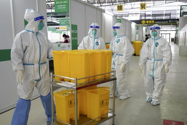 In this photo released by China's Xinhua News Agency, medical workers in protective suits walk at the Shanghai New International Expo Center, which has been converted to a quarantine facility for people with mild and symptomatic cases of COVID-19, in Shanghai, Friday, April 1, 2022. (Xinhua via AP)