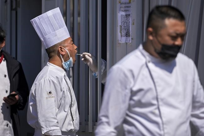A restaurant chef gets their throat swab taken at a coronavirus testing site, Sunday, April 3, 2022, in Beijing. COVID-19 cases in China's largest city of Shanghai are still rising as millions remain isolated at home under a sweeping lockdown. (AP Photo/Andy Wong)