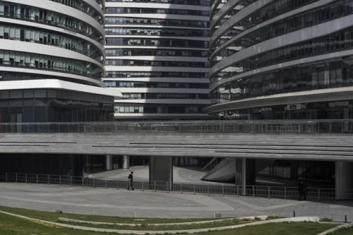 A security wearing a face mask to help protect from the coronavirus aligns the barricades at the Galaxy Soho commercial office building which was locked down for health monitoring following a COVID-19 case detected in the area, Tuesday, April 5, 2022, in Beijing. China has sent more than 10,000 health workers from across the country to Shanghai, including 2,000 military medical staff, as it struggles to stamp out a rapidly spreading COVID-19 outbreak in China's largest city. (AP Photo/Andy Wong)
