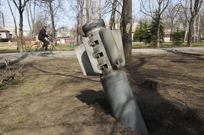 A man rides a bicycle as a tail of a missile sticks out in the city of Chuhuiv, Kharkiv region, Ukraine, Friday, April 8, 2022. (AP Photo/Andrew Marienko)