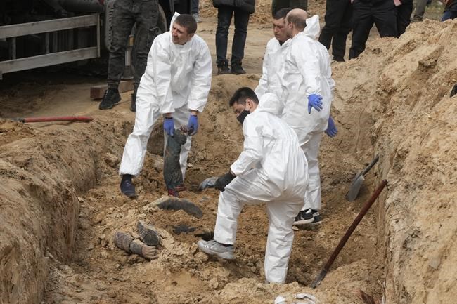 Men wearing protective gear exhume the bodies of killed civilians in Bucha, on the outskirts of Kyiv, Ukraine, Friday, April 8, 2022. An international organization formed to identify the dead and missing from the 1990s Balkan conflicts is preparing to send a team of forensics experts to Ukraine as the death toll mounts more than six weeks into the war caused by Russia's invasion. (AP Photo/Efrem Lukatsky)