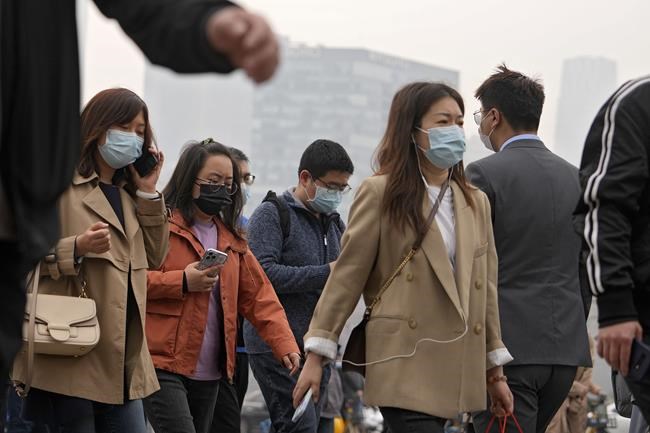 People wearing face masks to help protect from the coronavirus walk across a street during the morning rush hour, Monday, April 11, 2022, in Beijing. (AP Photo/Andy Wong)