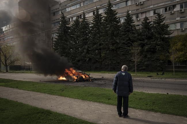 A man watches as a car burns with two people inside, after a Russian bombardment in Kharkiv, Ukraine, Thursday, April 21, 2022. (AP Photo/Felipe Dana)