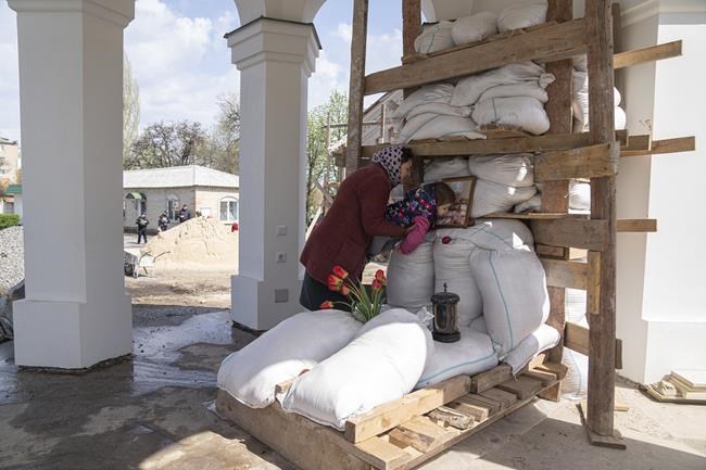 An Orthodox believer helps her daughter to kiss a photo of a priest, founder of All Saints church during the Easter celebration in Bahmut, eastern Ukraine, Sunday, April 24, 2022. (AP Photo/Evgeniy Maloletka)