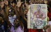 FILE - Soccer fans sing as they hold a poster of national soccer captain and goalkeeper Senzo Meyiwa during a memorial service held for three South African sports figures who died within days of each other at an indoor sports arena in downtown Johannesburg, South Africa, Oct. 30, 2014. Testimony began Monday April 25, 2022, in the trial of five men charged with murder in the shooting death of South Africa national soccer team captain Senzo Meyiwa eight years ago. (AP Photo/Themba Hadebe, File)
