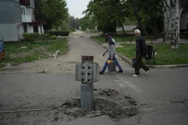 People walk past part of a rocket that sits wedged on the ground in Lysychansk, Luhansk region, Ukraine, Friday, May 13, 2022. (AP Photo/Leo Correa)