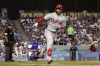 Philadelphia Phillies' Bryce Harper, right, gestures toward his dugout as he heads to first after hitting a three-run home run as Los Angeles Dodgers catcher Austin Barnes, center, kneels at first as home plate umpire Adrian Johnson watches during the third inning of a baseball game Saturday, May 14, 2022, in Los Angeles. (AP Photo/Mark J. Terrill)