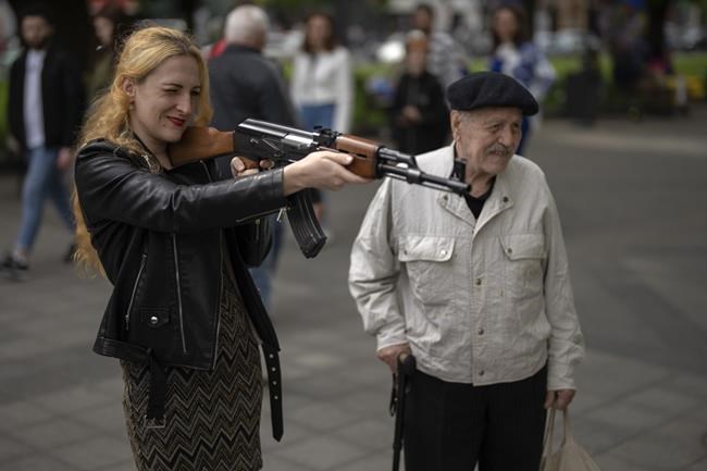 A woman uses a plastic Kalashnikov rifle to shoot balls at a portrait of Russian President Vladimir Putin, at a street attraction in the centre of Lviv, Ukraine on Saturday, May 14, 2022. (AP Photo/Emilio Morenatti)
