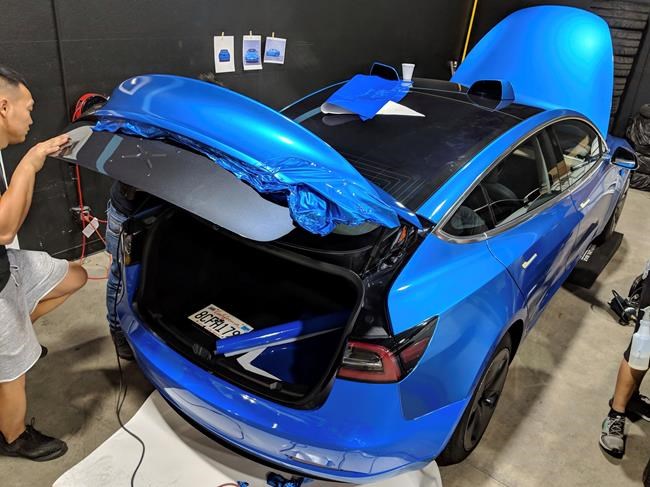 This photo provided by Edmunds shows a car wrap being installed on a Tesla Model 3. The job to apply this metallic light blue vinyl cost about $3,700 at a shop in Southern California. This included parts, labor and an optional ceramic coating for added durability. (Scott Jacobs/Courtesy of Edmunds via AP)