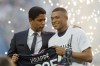 PSG President Nasser Al-Khelaifi, left, speaks to PSG's Kylian Mbappe who holds a shirt with his name and 2025 on it as it is announced he has signed a three year extension to his contract on the pitch ahead of the French League One soccer match between Paris Saint Germain and Metz at the Parc des Princes stadium in Paris, France, Saturday, May 21, 2022. (AP Photo/Michel Spingler)