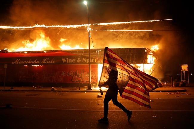 A protester carries a U.S. flag upside, a sign of distress, next to a burning building Thursday, May 28, 2020, in Minneapolis. Protests over the death of George Floyd, a black man who died in police custody Monday, broke out in Minneapolis for a third straight night. THE CANADIAN PRESS/AP-Julio Cortez