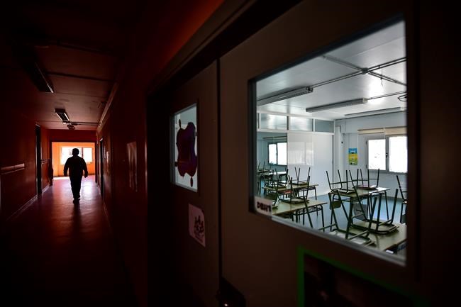 A teacher walks along a hallway of an empty public school in small Spanish Basque village of Labastida, around 45 kms (24,85 miles) from Vitoria, northern Spain, Wednesday, March 11, 2020. Spain's health minister on Monday announced a sharp spike in coronavirus cases in and around the national capital, and said all schools in the region, including kindergartens and universities, and the same in the Spanish Basque city of Vitoria, will close for two weeks.For most people, the new coronavirus causes only mild or moderate symptoms, such as fever and cough. For some, especially older adults and people with existing health problems, it can cause more severe illness, including pneumonia. (AP Photo/Alvaro Barrientos)