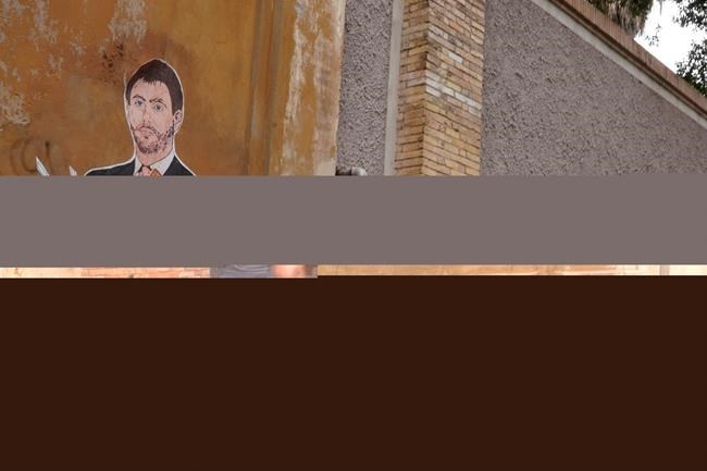 A passerby stops to take a picture of a murales depicting Juventus president Andrea Agnelli making a hole in a football with a knife, in Rome, Thursday, April 22, 2021. Juventus was one of the three Italian soccer clubs among the founding members of the now defunct project to give life to a