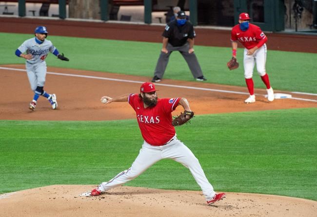 Texas Rangers starting pitcher Lance Lynn, foreground, delivers against the Los Angeles Dodgers as Dodgers' Mookie Betts, back left, leads off and Rangers third baseman Todd Frazier, right, and first base umpire Marvin Hudson look on during the first inning of a baseball game Saturday, Aug. 29, 2020, in Arlington, Texas. (AP Photo/Jeffrey McWhorter)