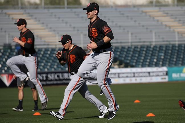 San Francisco Giants catcher Buster Posey, right, jumps in the air as he warms up with teammates during spring training baseball workouts for pitchers and catchers Wednesday, Feb. 12, 2020, in Scottsdale, Ariz. (AP Photo/Ross D. Franklin)