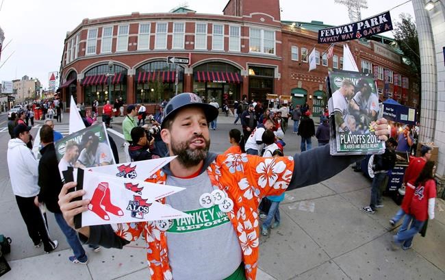 FILE - In this Oct. 19, 2013, file photo, Tim Lampa hawks programs and Boston Red Sox pennants outside Fenway Park before Game 6 of the American League baseball championship series between the Red Sox and the Detroit Tigers in Boston. Ballpark area businesses are struggling during the 2020 season while fans are not in attendance due to the COVID-19 pandemic. (AP Photo/Charlie Riedel, File)