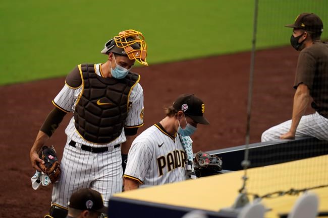 San Diego Padres starting pitcher Garrett Richards, center, walks into the dugout followed by catcher Austin Nola after the team's baseball game against the San Francisco Giants was postponed Friday, Sept. 11, 2020, in San Diego, minutes before the scheduled first pitch after someone in the Giants organization tested positive for COVID-19. (AP Photo/Gregory Bull)