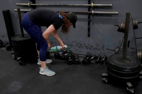 FILE - In a Friday, April 24, 2020 file photo, Alexis Garrod, CrossFit Potrero Hill partner and head coach, cleans off weight training equipment in an empty gym, which closed for shelter in place orders over COVID-19 concerns, in San Francisco. Reebok says it has cut ties with CrossFit chief executive and founder invoked George Floyd’s name in a Twitter post chastising a health group for saying that racism was a public health problem. (AP Photo/Jeff Chiu, File)