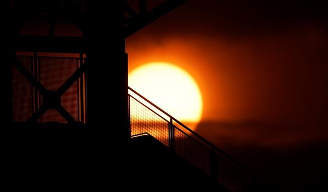 As smoke from wildland fires from across the American West fills the sky, the sun casts an orange glow as it sets, with the stands of Coors Field in the foreground during the first inning of a baseball game between the Los Angeles Dodgers and the Colorado Rockies on Friday, Sept. 18, 2020, in Denver. (AP Photo/David Zalubowski)
