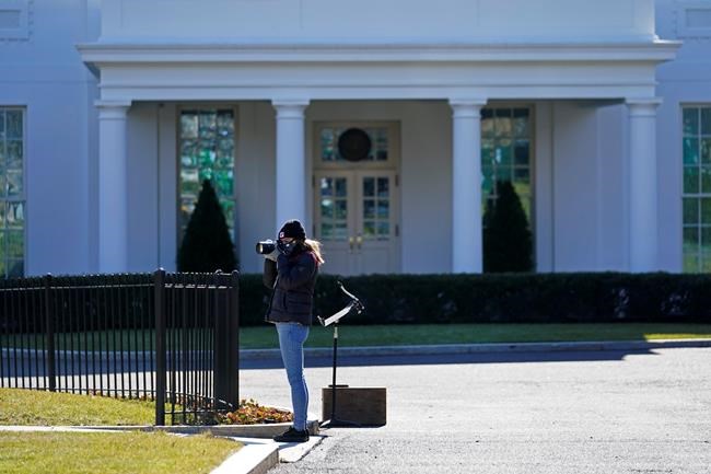 Freelance photographer Allison Dinner photographs workers setting up lights, in front the West Wing of the White House, Tuesday, Jan. 19, 2021, in Washington. On President Donald Trump's last full day in office, there was an eerie quiet, with no public events scheduled, his last event being Jan. 12, seven days earlier. (AP Photo/Gerald Herbert)