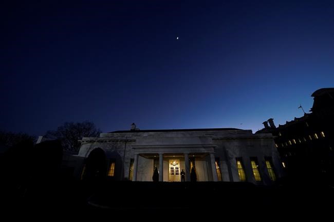 The moon rises over the West Wing of the White House, on President Donald Trump's last day in office, Tuesday, Jan. 19, 2021, in Washington. The Marine guard at the entrance signifies the president is in the Oval Office. (AP Photo/Gerald Herbert)