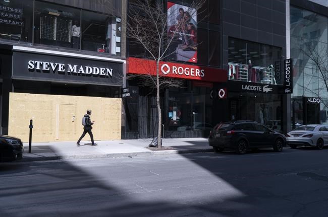 A pedestrian walks past a boarded store on Montreal's Ste-Catherine street, on Tuesday, April 28, 2020. THE CANADIAN PRESS/Paul Chiasson