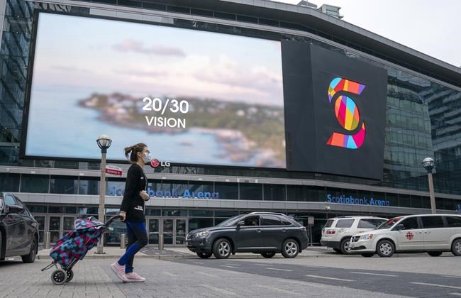 A woman wearing a mask pulls her suitcase in front of Scotiabank Arena where both the Raptors and Maple Leafs play in Toronto on Thursday, March 12, 2020. Toronto and Edmonton are on the verge of being picked as hub cities for the NHL's resumption of play, according to multiple reports. THE CANADIAN PRESS/Frank Gunn