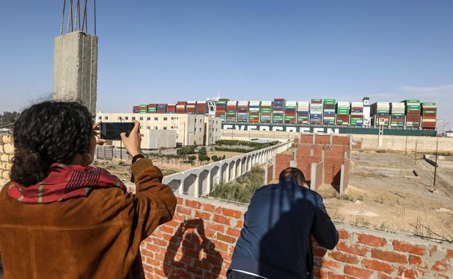 People watch Ever Given, a Panama-flagged cargo ship, that has been stuck sideways and blocked traffic in Egypt's Suez Canal, move past after it was set free by salvage teams, Monday, March 29, 2021. (AP Photo/Mohamed Elshahed)