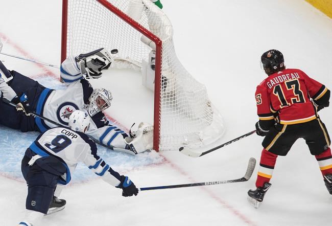 Winnipeg Jets goalie Connor Hellebuyck (37) is scored on by Calgary Flames' Johnny Gaudreau (13) as Jets' Andrew Copp defends during second period NHL qualifying round game action in Edmonton, on Saturday August 1, 2020. THE CANADIAN PRESS/Jason Franson