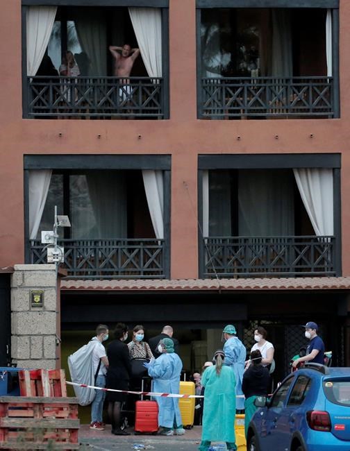 Health personnel wearing protection clothing assist guests as they leave the H10 Costa Adeje Palace hotel in La Caleta, in the Canary Island of Tenerife, Spain, Friday Feb. 28, 2020. Some guests have started to leave the locked down hotel after undergoing screening for the new virus that is infecting hundreds worldwide. (AP Photo/Joan Mateu)