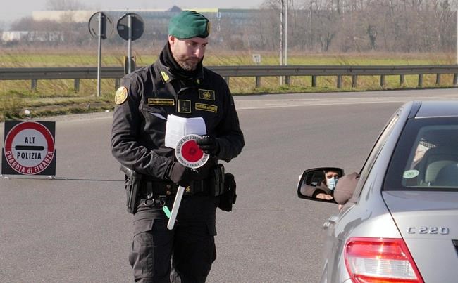 An Italian tax police officer talks to a man wearing a sanitary mask at a road block set in Casalpusterlengo, Northern Italy, Monday, Feb. 24, 2020. Italy scrambled to check the spread of Europe's first major outbreak of the new viral disease amid rapidly rising numbers of infections and a third death. Road blocks were set up in at least some of 10 towns in Lombardy at the epicenter of the outbreak, including in Casalpusterlengo, to keep people from leaving or arriving. (AP Photo/Paolo Santalucia)