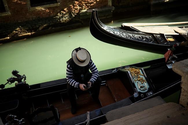 A gondolier looks at his smartphone as he waits for clients in Venice, Italy, Friday, Feb. 28, 2020. Authorities in Italy decided to re-open schools and museums in some of the areas less hard-hit by the coronavirus outbreak in the country which has the most cases outside of Asia, as Italians on Friday yearned for a return to normal life even amid fears that the outbreak could plunge the country's economy into recession. (AP Photo/Francisco Seco)