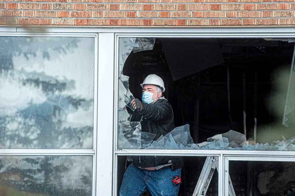 A worker pulls glass out of a broken window on the first floor of St James Collegiate Sunday afternoon after a fire broke out Sunday morning. (Mike Sudoma / Winnipeg Free Press)