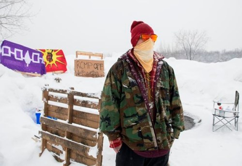 A member of the Mohawk community is shown on the Kahnawake reserve near a Canadian Pacific rail track south of Montreal, Monday, February 10, 2020 to stand in solidarity with protesters opposed to a pipeline project in northwestern B.C. THE CANADIAN PRESS/Graham Hughes