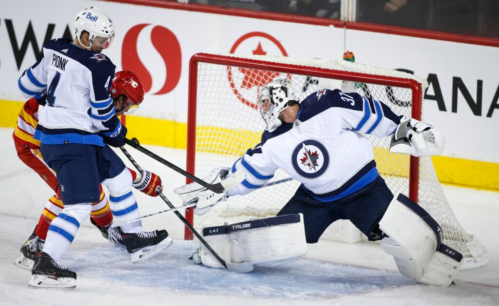 CP
Connor Hellebuyck and Neal Pionk keep Calgary's Rasmus Andersson from putting the puck in the net during the second period. (Jeff McIntosh / The Canadian Press)