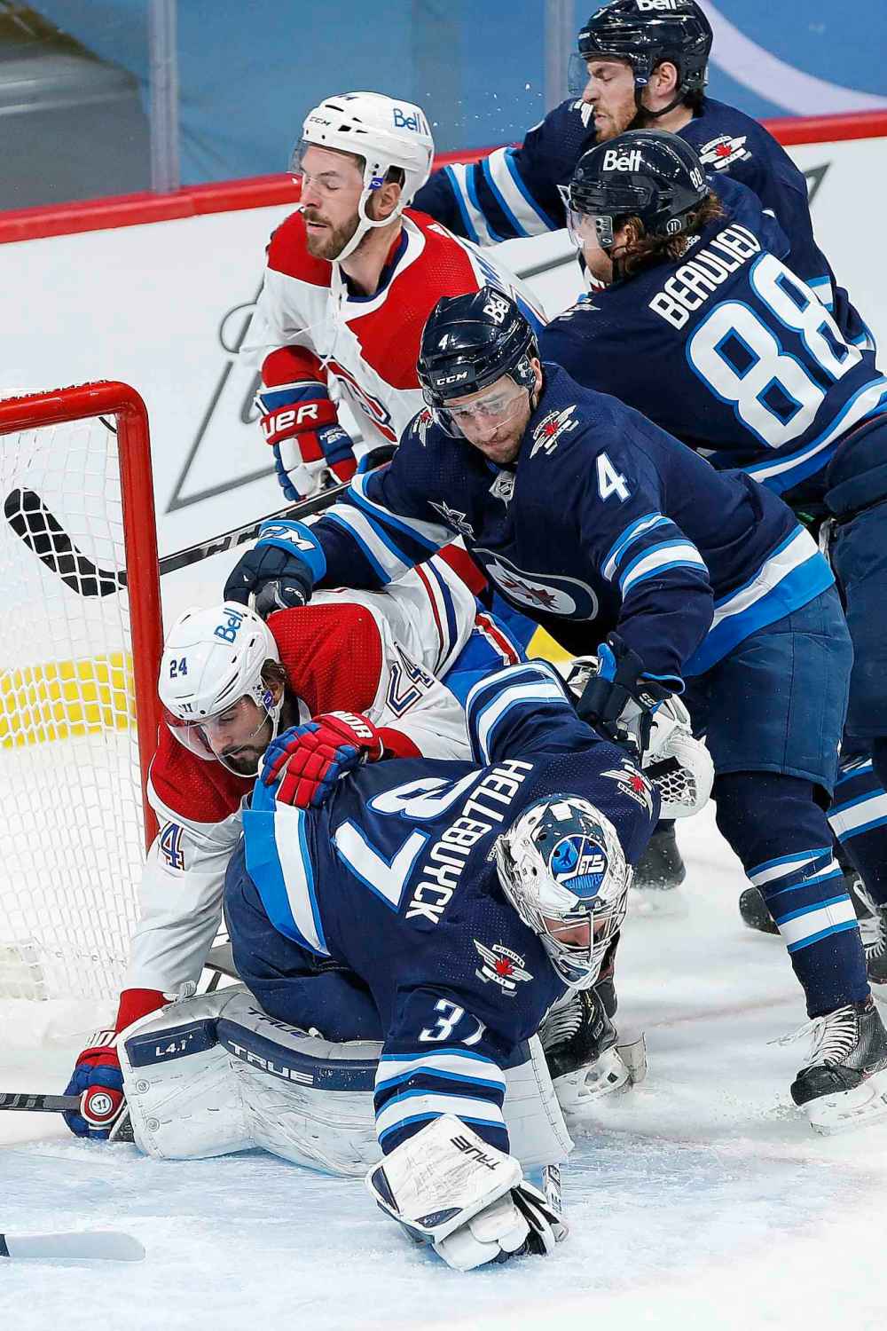 Winnipeg Jets goaltender Connor Hellebuyck (37) dives on the rebound as Montreal Canadiens' Phillip Danault (24) crashes into him and Jets' Neal Pionk (4) defends during the second period. (John Woods / The Canadian Press)