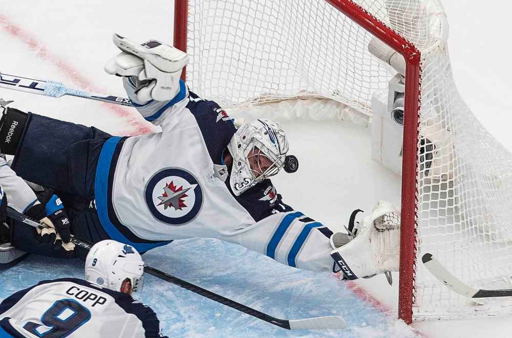 Winnipeg Jets goalie Connor Hellebuyck (37) is scored on by Calgary Flames' Johnny Gaudreau as Jets' Andrew Copp defends during the second period. (Jason Franson / The Canadian Press)
