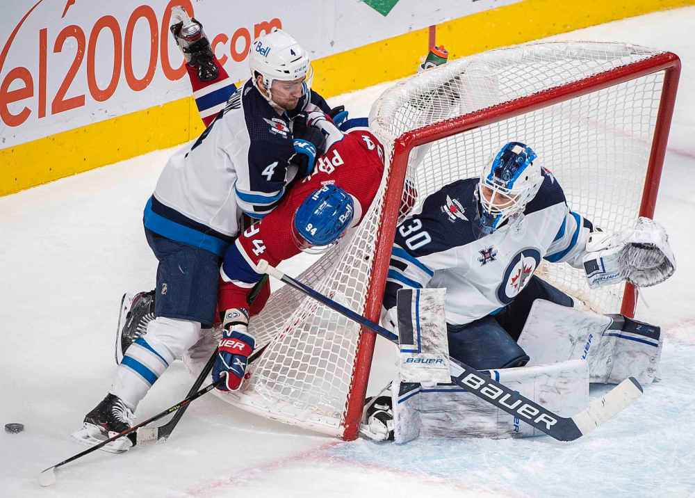 Winnipeg Jets goaltender Laurent Brossoit looks on as Jets’ Neal Pionk (4) upends Montreal Canadiens’ Corey Perry (94) during the third period . (Graham Hughes / The Canadian Press)