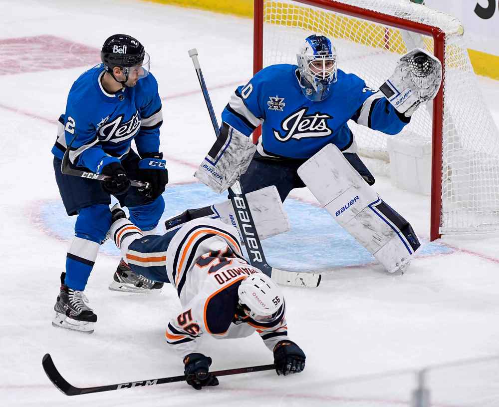 Winnipeg Jets goaltender Laurent Brossoit (30) makes a save as Edmonton Oilers’ Kailer Yamamoto (56) is dumped by Dylan DeMelo (2) in front of the net during the first period. (Fred Greenslade / The Canadian Press)
