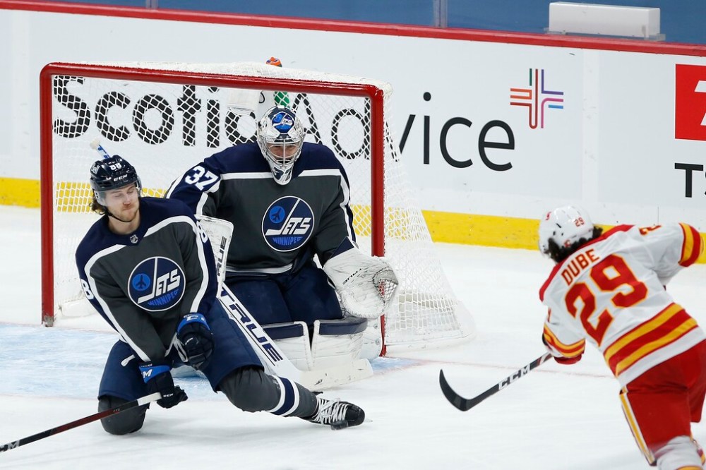 Winnipeg Jets' Nathan Beaulieu blocks a shot by Calgary Flames' Dillon Dube in front of goaltender Connor Hellebuyck during the third period of the Jets 4-1 win in Winnipeg on Thursday. THE CANADIAN PRESS/John Woods