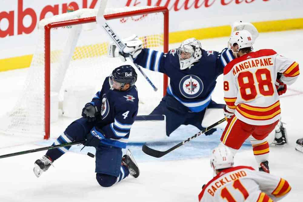 CP
Winnipeg Jets' Neal Pionk blocks a shot from Calgary Flames' Mikael Backlund as goaltender Connor Hellebuyck stretches to make the save in the second period. THE CANADIAN PRESS/John Woods
