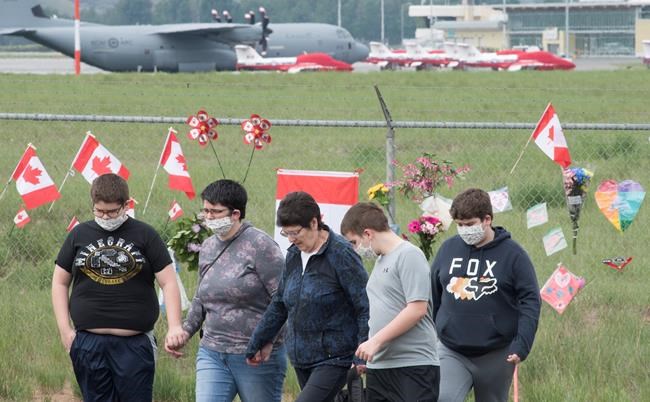 The Canadian Forces Snowbirds jets are seen in the background as a family pays their respects in Kamloops, B.C., Monday, May 18, 2020. Capt. Jenn Casey died Sunday after the Snowbirds jet she was in crashed shortly after takeoff. The pilot of the aircraft is in hospital with serious injuries. THE CANADIAN PRESS/Jonathan Hayward