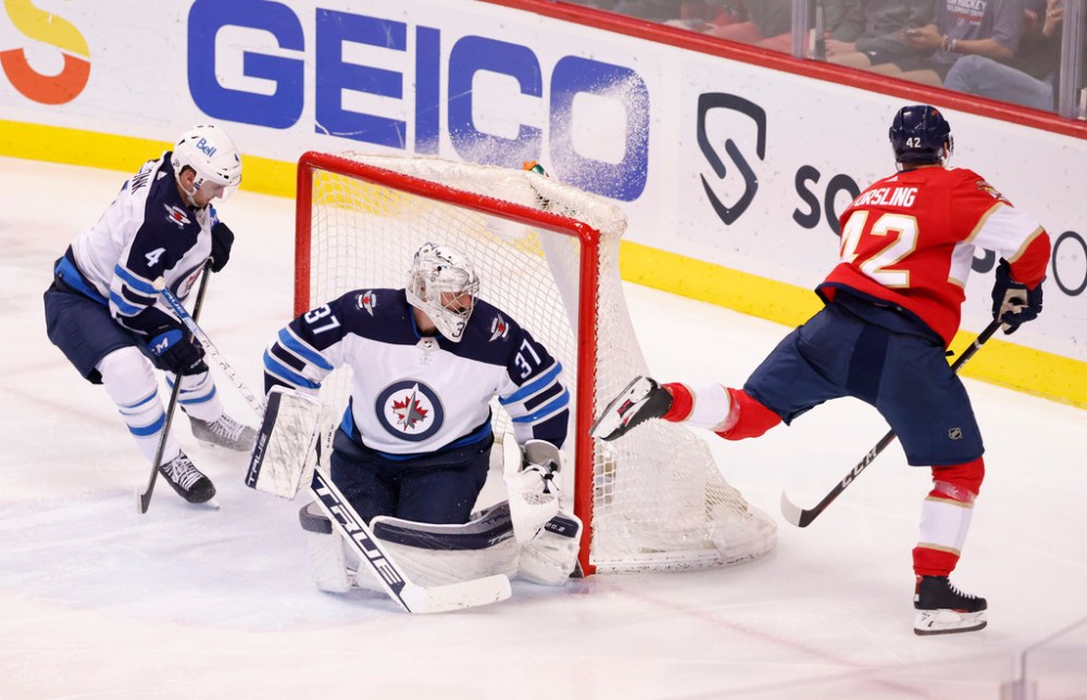 Florida Panthers defenseman Gustav Forsling (42) scores a goal against Winnipeg Jets goaltender Connor Hellebuyck (37) as Jets defenseman Neal Pionk (4) looks on during the second period of an NHL hockey game Friday, April 15, 2022, in Sunrise, Fla. (AP Photo/Reinhold Matay)