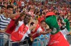 FILE - In this Saturday, July 18, 2015 file photo, fans pose for pictures with Arsenal's mascot Gunnersaurus ahead of their team's soccer match against Everton for the Barclays Asia Trophy in Singapore. Out-of-favor Arsenal playmaker Mesut Ozil wants to save Gunnersaurus from extinction. Ozil expressed sadness Tuesday Oct. 6, 2020, after discovering that Jerry Quy — the man who fills the Arsenal dinosaur mascot outcut — had been made redundant by the London club after 27 years. (AP Photo/Joseph Nair, File)