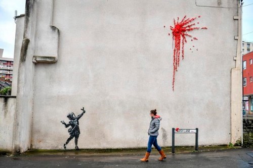 A woman walks past a new artwork on the side of a house in Bristol, England, Thursday Feb. 13, 2020, which has been confirmed as the work of street artist Banksy. (Ben Birchall/PA via AP)